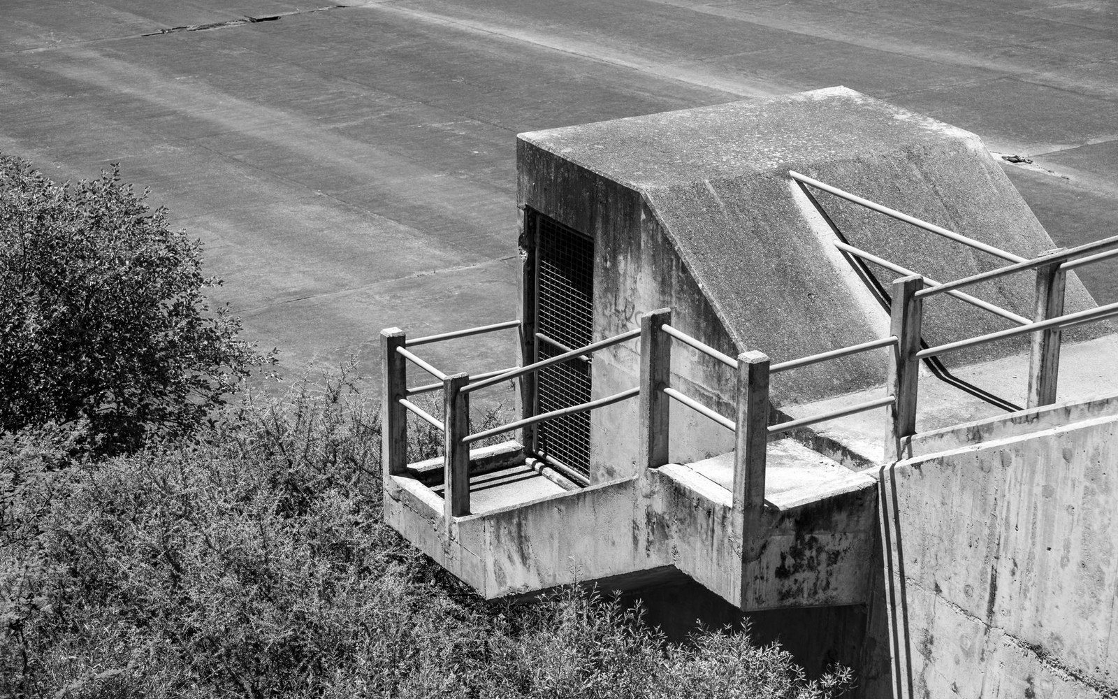Englewood dam outlet works at low angle, two maintenance staff on the concrete apron, full embankment visible behind them