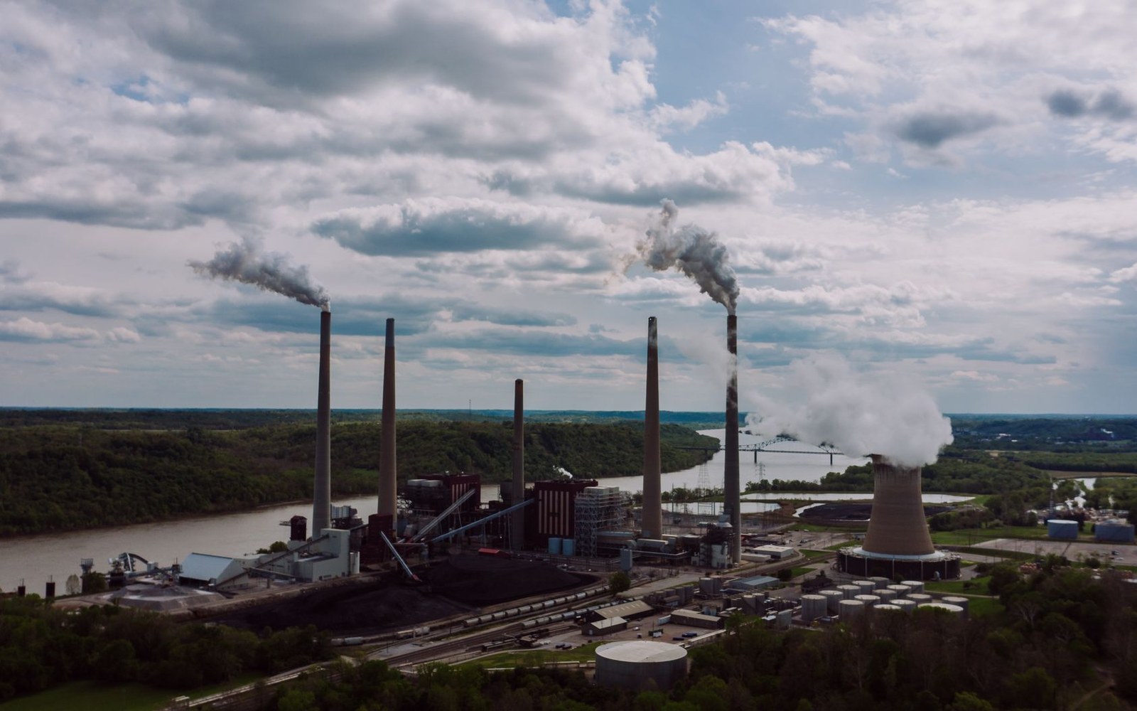 Coal-fired power plant with tall smokestacks and cooling tower emitting steam beside a river