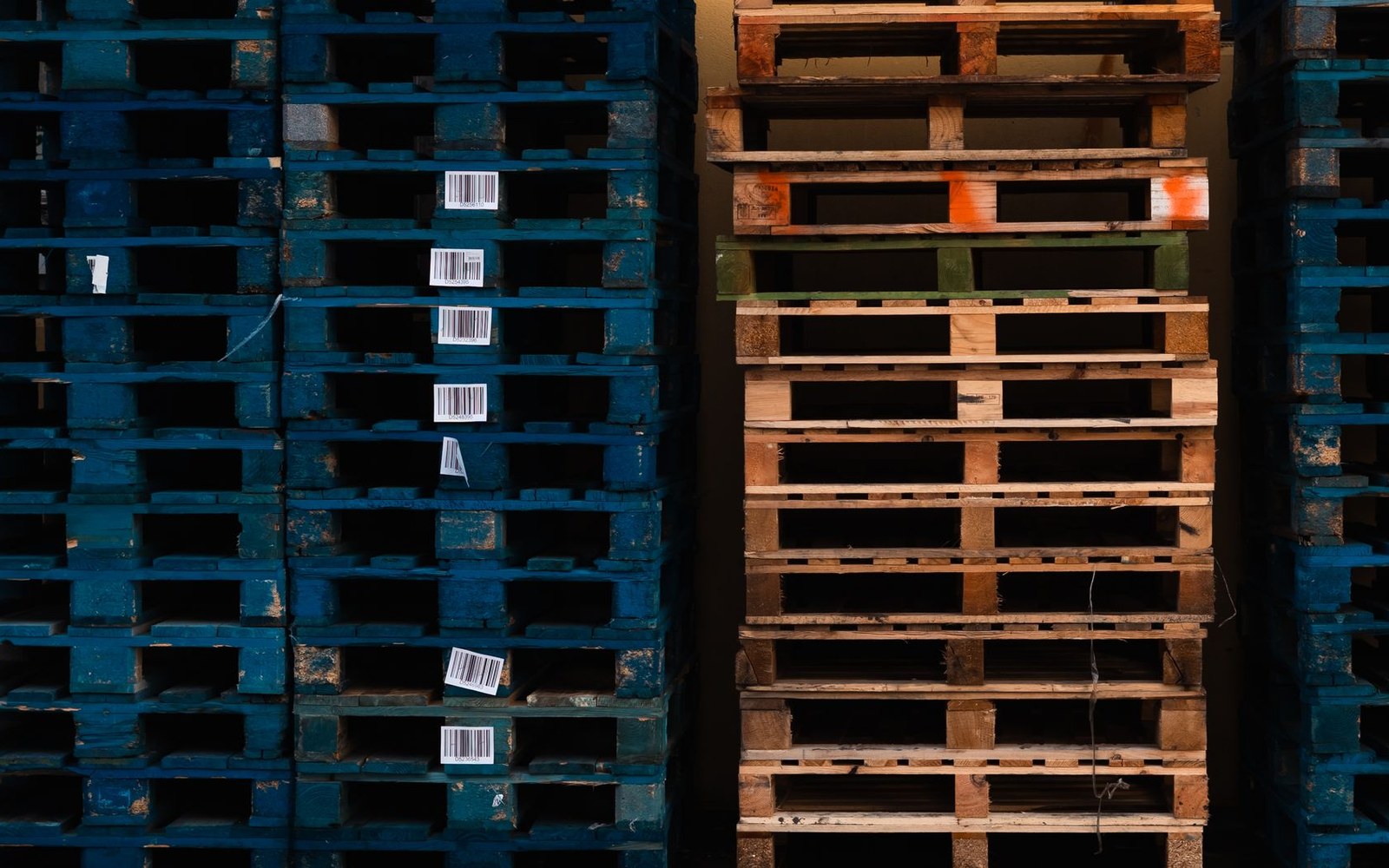 Stacks of blue-painted and unpainted wooden pallets with barcode labels attached