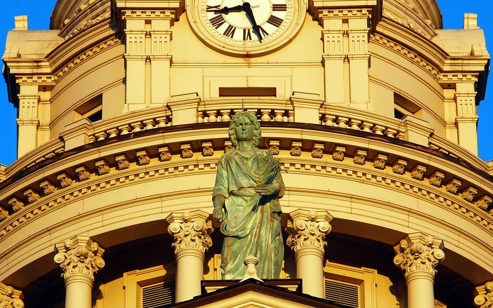 A weathered bronze statue stands atop the domed courthouse below its clock tower