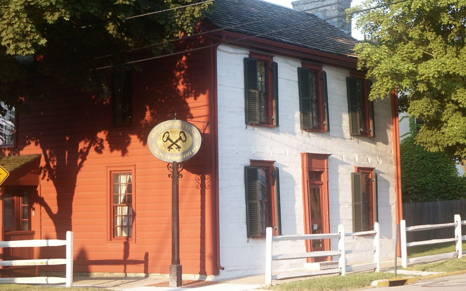 Two-story white and orange building with dark shutters behind a white picket fence