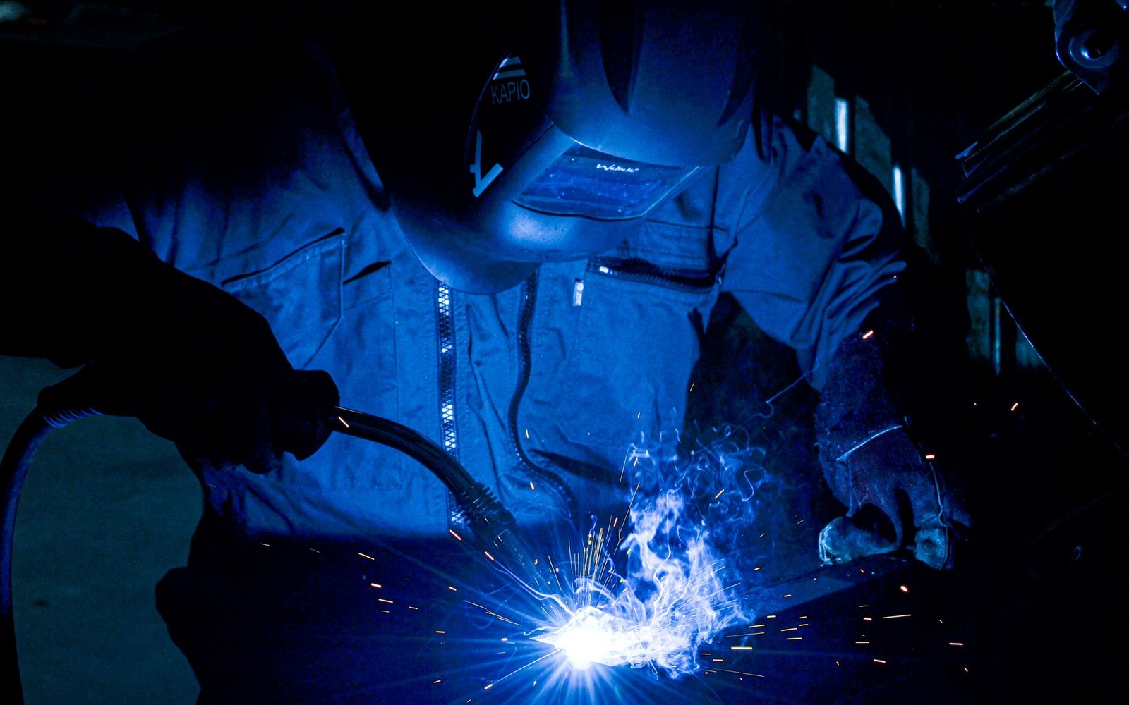 Welder in protective helmet and gloves creates bright sparks while joining metal