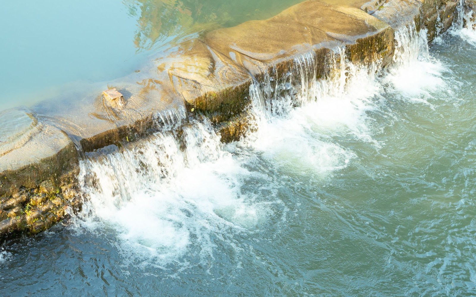 The ungated conduit outlet at Taylorsville dam from the downstream apron, an adult standing at the opening so the concrete reads at true scale, stain line visible above
